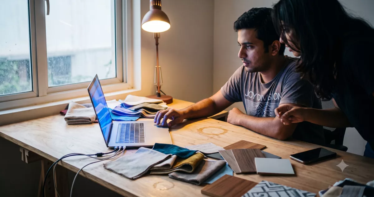 Marketer checking a redirect spreadsheet on dual monitors while planning a website redesign without losing SEO at a textile studio desk